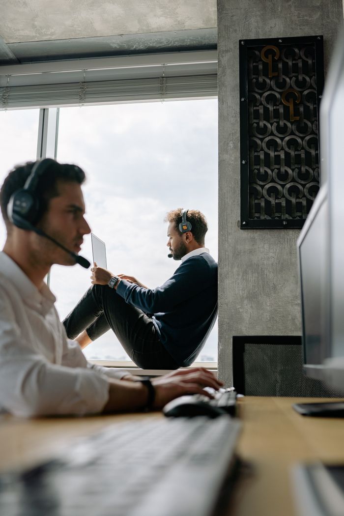 Mastering the First Impression: Your intriguing post title goes here Two men in an office setting wearing headphones and working, showing focused and productive workspace.